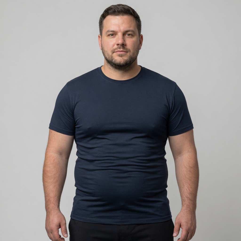A male model wearing a standard, tight-fitting dark t-shirt. The thin fabric clings to the body, emphasizing the midsection and demonstrating a common unflattering fit that lacks structural support.